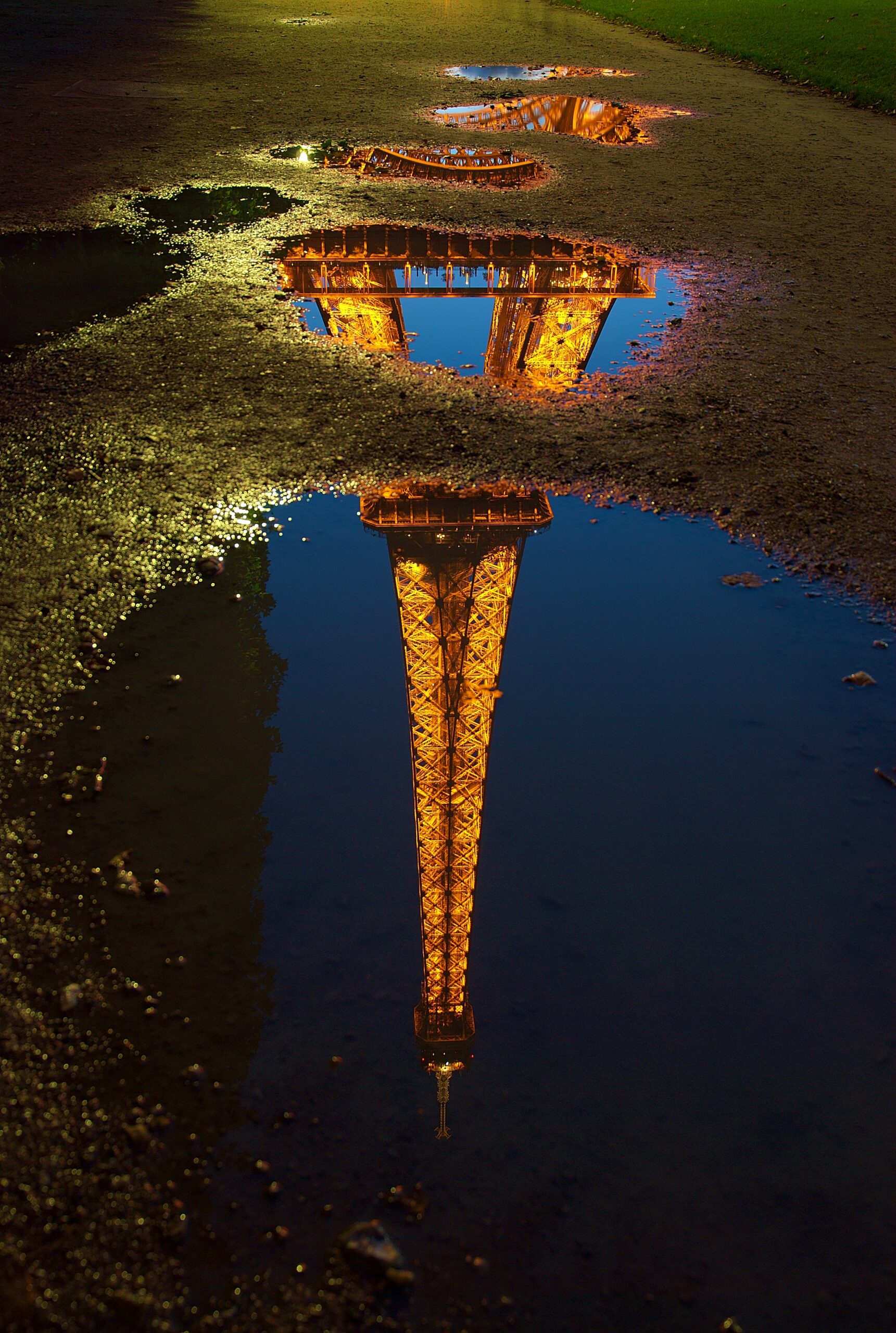 A reflection of the lit-up Eiffel Tower in a water pond